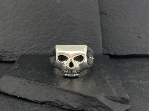 A silver skull ring with black eye sockets on a dark slate surface.