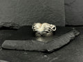 Elegant silver ring with an intricate, flowing design on a dark slate surface.