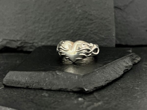 Elegant silver ring with an intricate, flowing design on a dark slate surface.