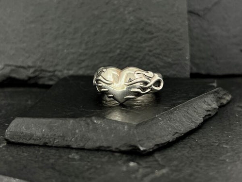 Elegant silver ring with an intricate, flowing design on a dark slate surface.