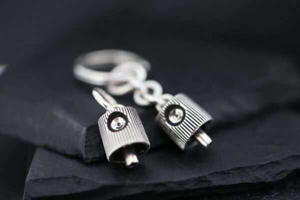 Close-up of two silver robot keychains on a dark surface.