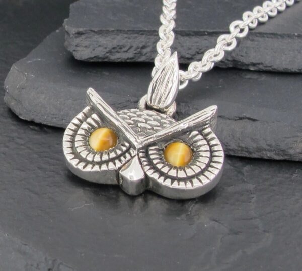 Silver owl pendant with yellow eyes on a chain.