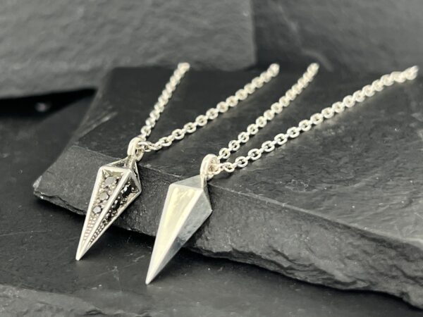 Two geometric pendant necklaces displayed on dark slate.