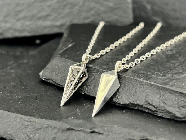 Two elegant silver arrowhead pendants on chains displayed on dark stone.