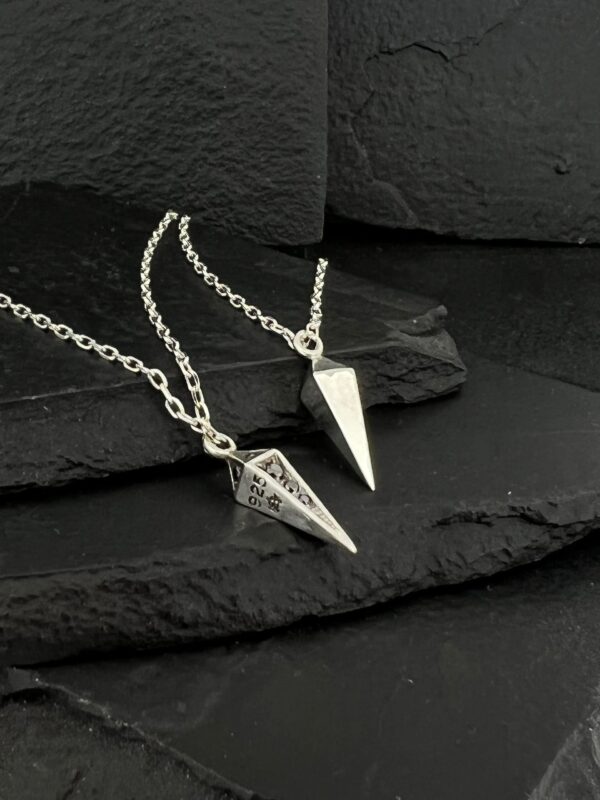 Two silver pendulums on chains placed on black slate.