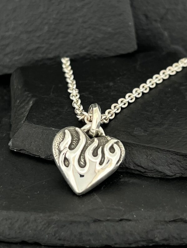 Silver heart pendant with flame design on chain.