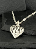 Silver heart pendant with flame design on chain.