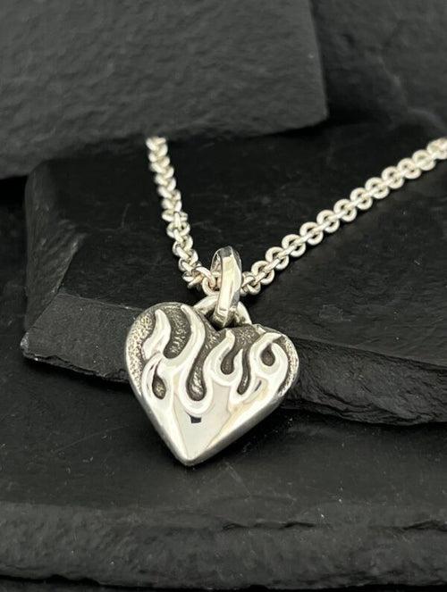 Silver heart pendant with flame design on chain.