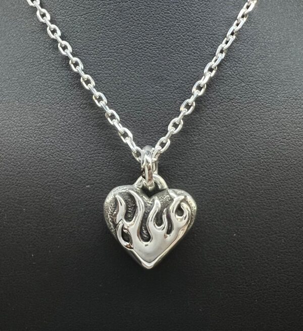Silver heart pendant with flame design on a chain.
