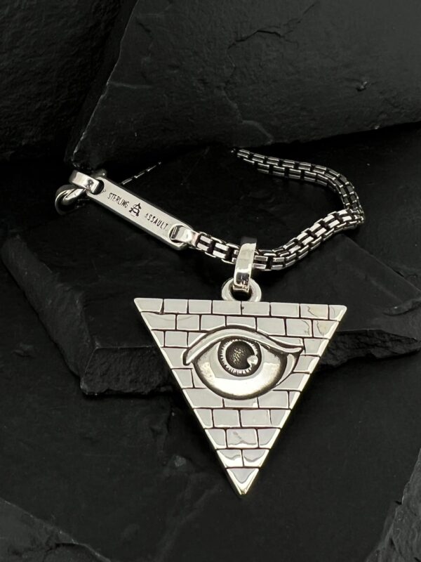 Silver triangular pendant with an eye and brick pattern on a chain.