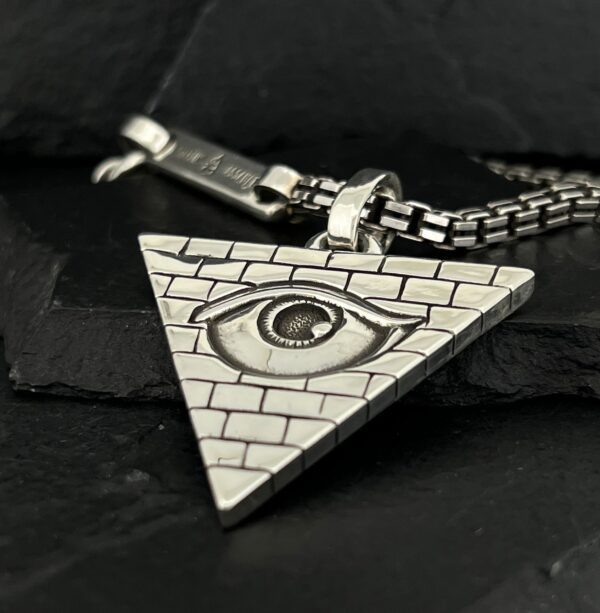Triangular pendant with an eye symbol and brick pattern on a chain.