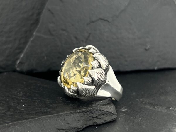 A silver ring with a large yellow gemstone, styled like a flower.