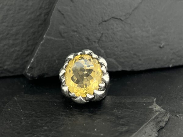 Close-up of a silver and yellow gemstone ring on a dark slate surface.