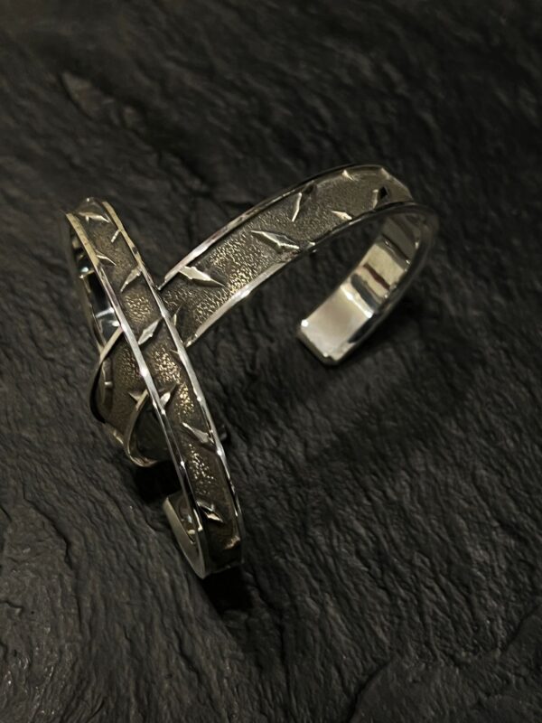 Close-up of a rustic metal bracelet on a dark textured surface.