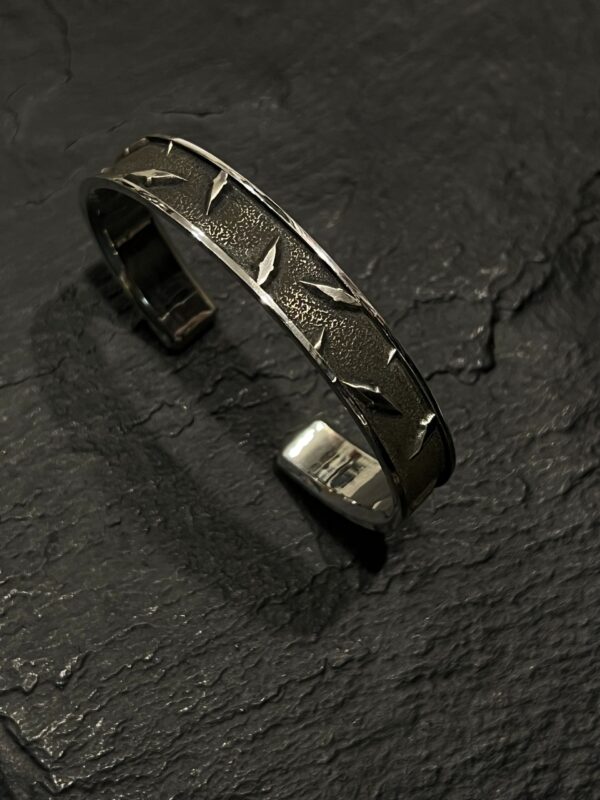 Silver cuff bracelet with star engravings on a dark surface.