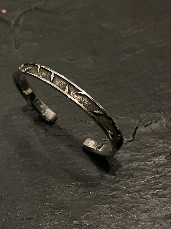 A silver cuff bracelet with geometric patterns on a dark surface.