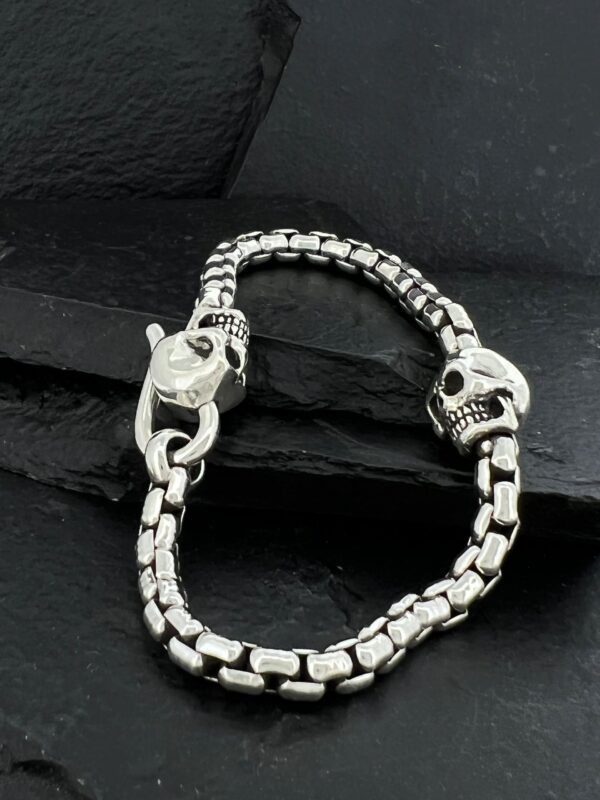 Silver bracelet with skull and clasp details on a dark surface.