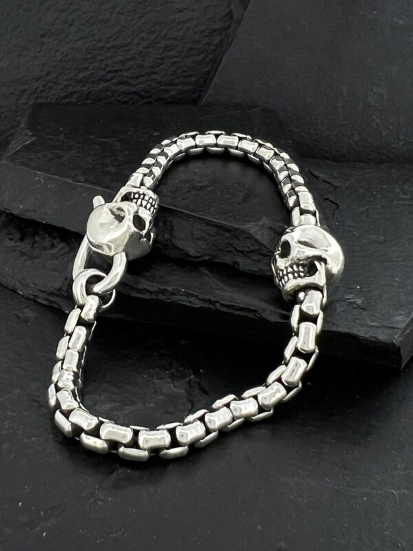 Silver bracelet with skull-shaped clasps on a dark surface.