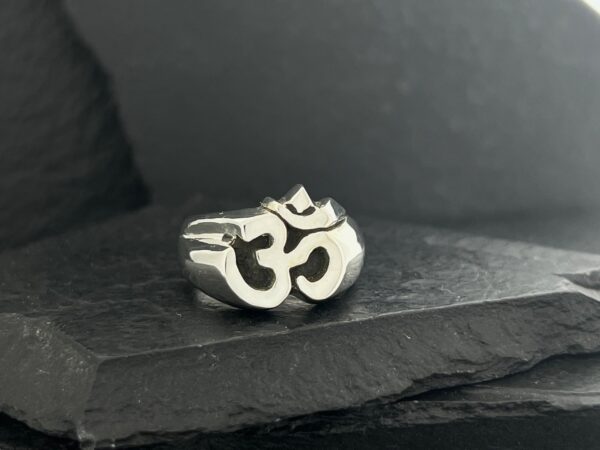 A silver ring featuring the Om symbol on a dark surface.