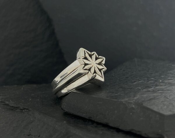 Elegant silver ring with a star-shaped design on a dark surface.
