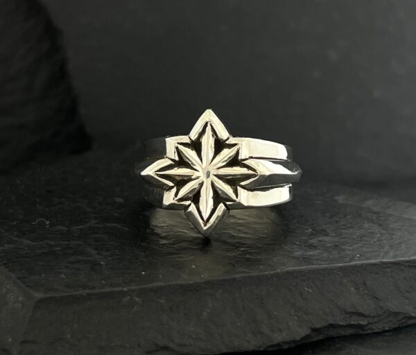 Silver ring with a star-shaped geometric design on black background.