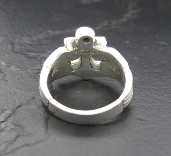 Silver ring with a unique cross-shaped design on a dark surface.