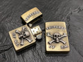 Two skull-themed brass lighters with inscriptions on a black surface.