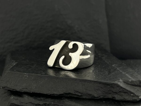 A silver ring featuring the number 13 on a dark surface.