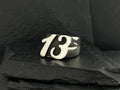 A silver ring featuring the number 13 on a dark surface.