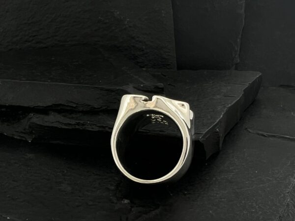 Silver ring with a skull design on black textured background.