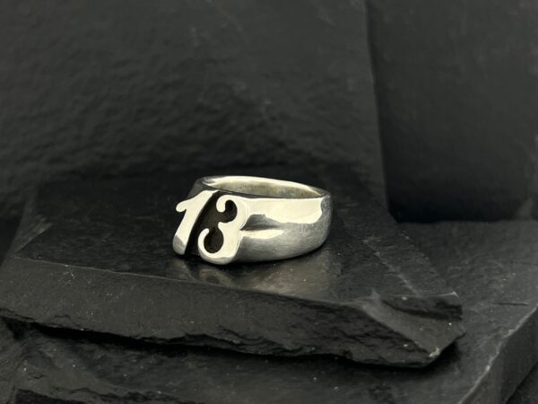 Silver ring featuring the number 13 on a dark stone surface.
