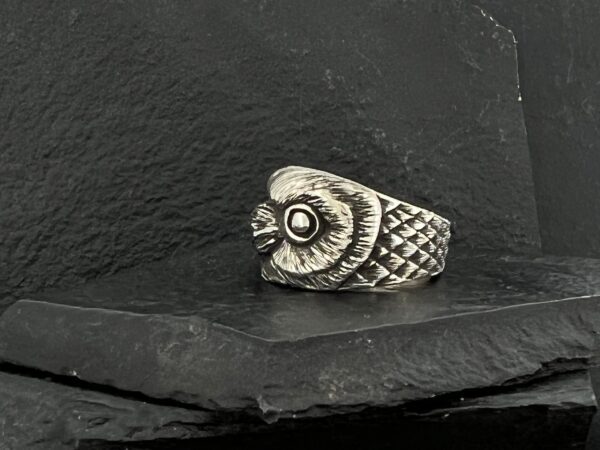 A detailed silver owl-shaped ring on a dark stone surface.
