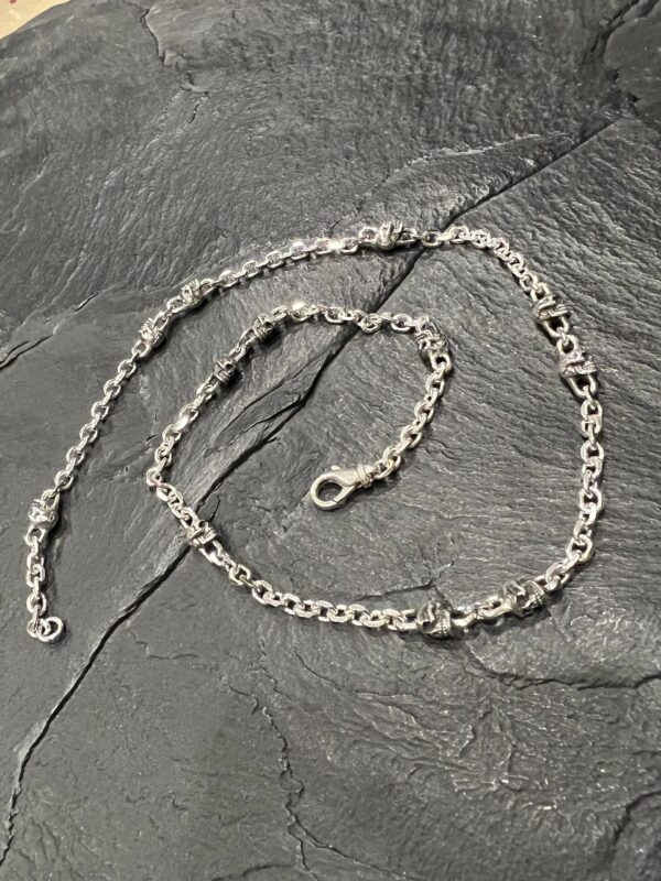 Silver chain necklace placed on a dark stone surface.