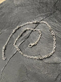 Silver chain necklace placed on a dark stone surface.