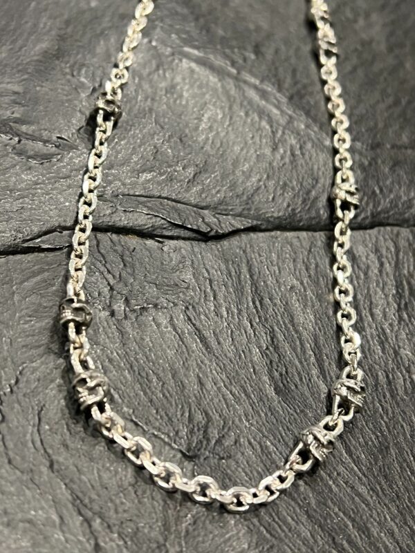 Silver chain necklace with intricate links on a textured surface.