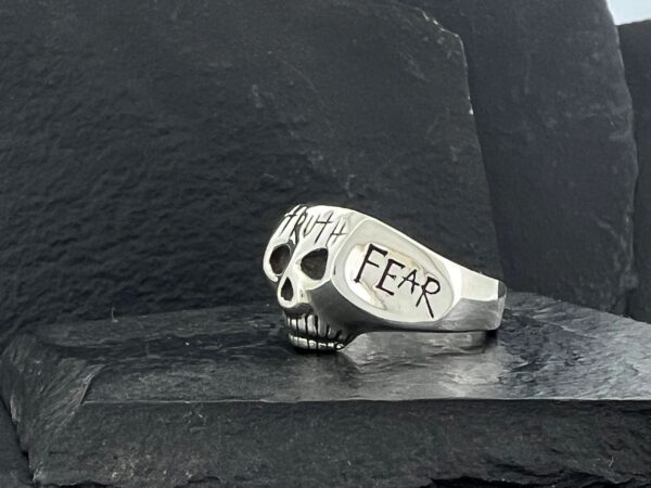 A silver skull ring engraved with the word 'FEAR'.