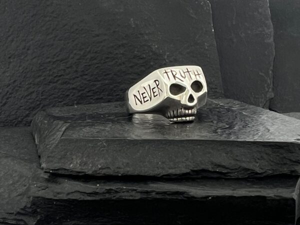 Silver skull ring engraved with 'NEVER TRUST'.