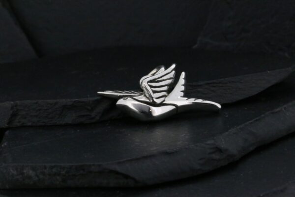 A silver bird brooch on a dark textured surface.