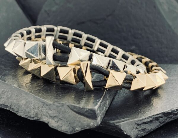 Close-up of a pyramid-studded leather bracelet on a stone surface.