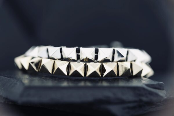 Close-up of silver pyramid-studded bracelets on a dark surface.