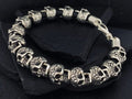 Silver bracelet with skull designs on a dark surface.
