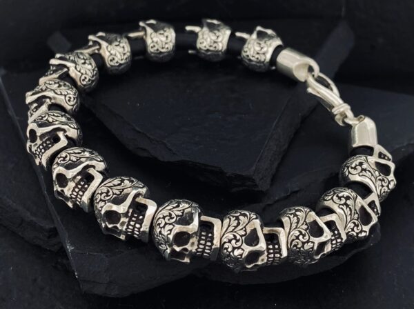 Silver bracelet with skull designs on a dark surface.