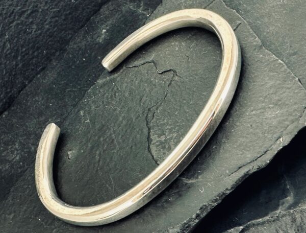 A sleek silver cuff bracelet on a dark slate surface.