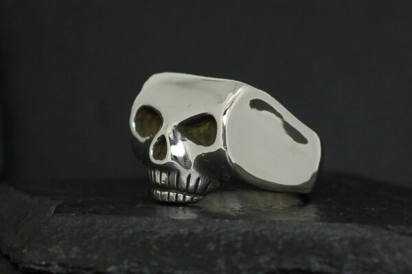 A metallic skull-shaped ring with dark eye sockets on a dark surface.