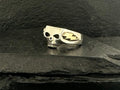 A silver ring featuring a skull and a spade symbol on a black stone surface.