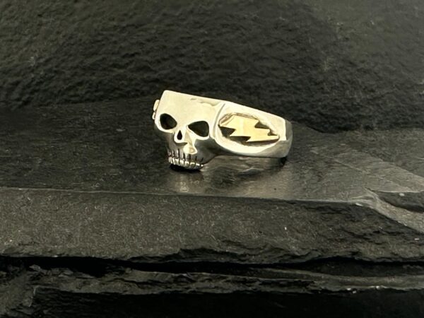 A silver ring featuring a skull and a spade symbol on a black stone surface.