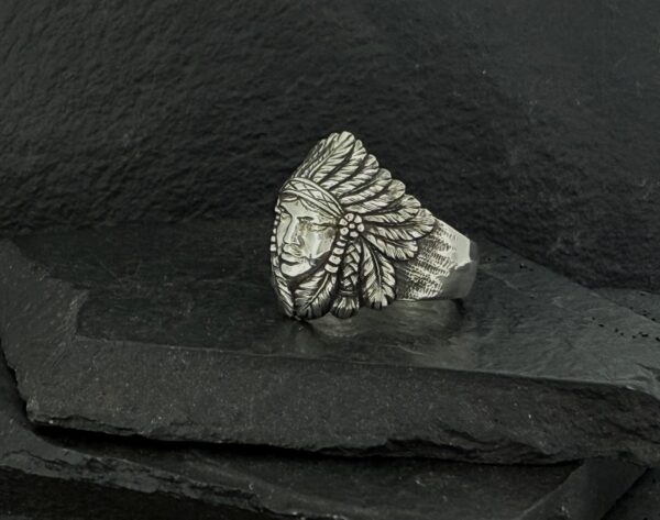 Silver ring with a Native American chief design on a dark stone background.