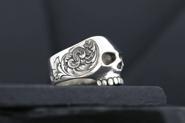 A detailed silver skull ring with intricate floral engravings.