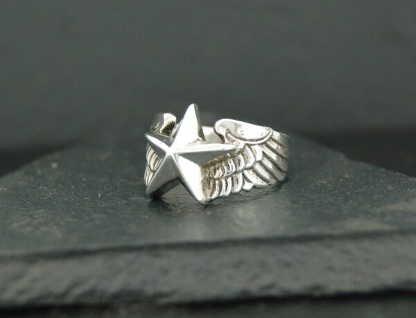 Silver ring with a star and wing design on a dark surface.