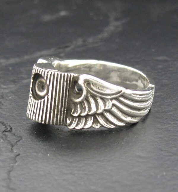 Silver ring with wing design and screw detail on a dark surface.
